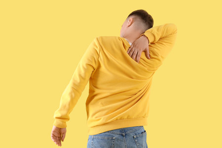 Young man suffering from back pain on color backgroundの写真素材