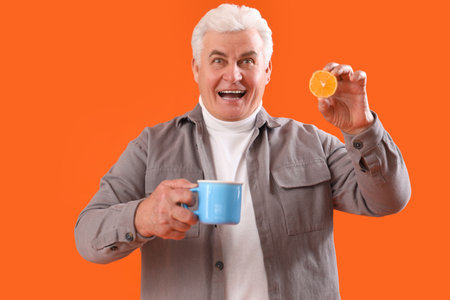 Mature man with cup of tea and lemon on orange backgroundの写真素材