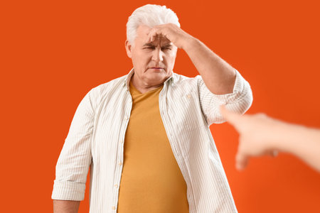 Woman pointing at mature man on orange background. Accusation conceptの写真素材