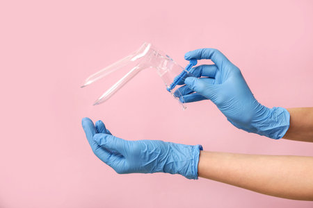 Doctor hands in medical gloves with gynecological speculum on pink backgroundの写真素材