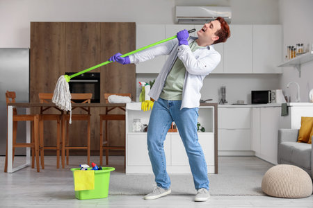 Young man having fun with floor mop in kitchen