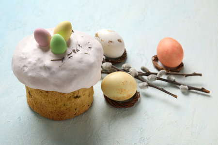 Easter cake, willow branches and painted eggs on light blue background