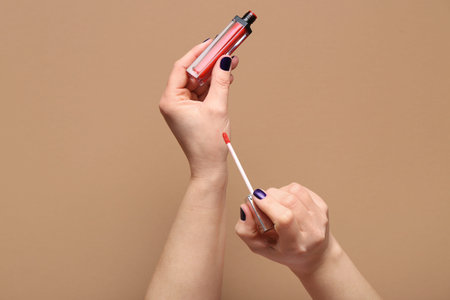 Female hands with red liquid lipstick on brown background
