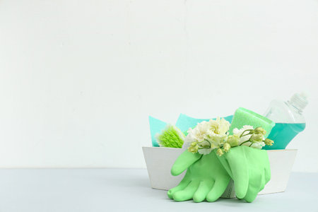 Basket with cleaning supplies, tools and spring flowers on white background