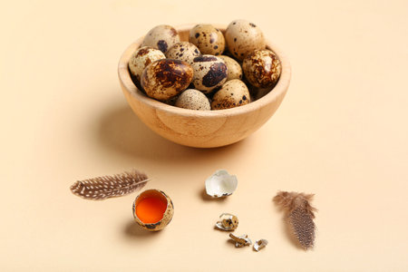 Wooden bowl with fresh quail eggs and feathers on beige background