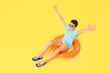 Cute little happy boy with ring buoy and goggles sitting on yellow background