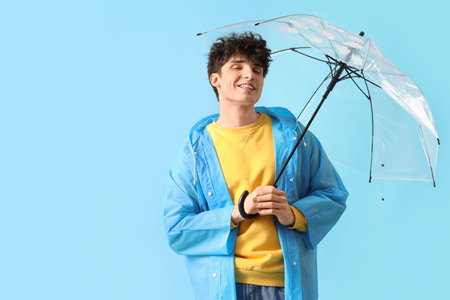 Young man in raincoat with umbrella on blue backgroundの写真素材