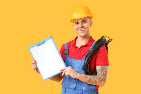 Young male electrician with cable and blank clipboard on yellow backgroundの写真素材