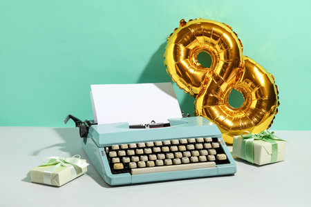 Vintage typewriter, gift boxes and balloon for Women's Day on white table against turquoise backgroundの写真素材