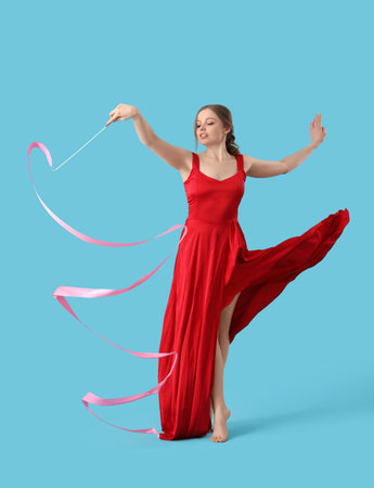 Beautiful young woman with ribbon dancing on blue backgroundの写真素材