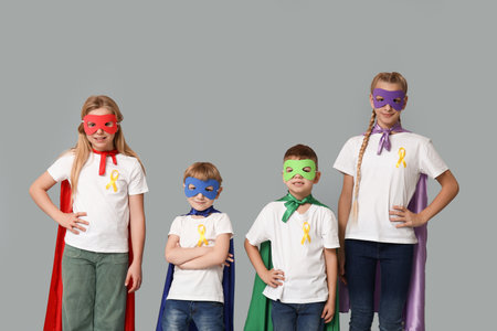 Group of kids in superhero costumes with yellow ribbons on gray background. International Childhood Cancer Dayの写真素材