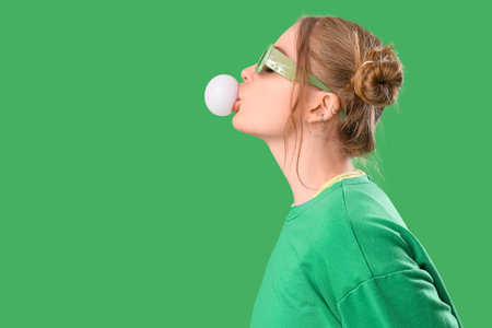 Beautiful young woman in stylish outfit chewing gum on green backgroundの写真素材
