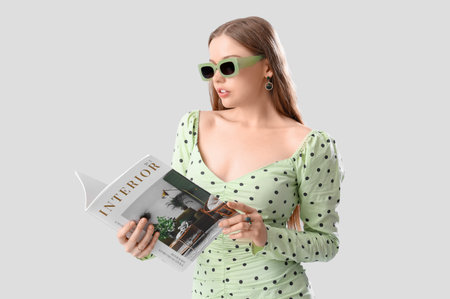Beautiful young woman in stylish outfit with magazine on gray backgroundの写真素材