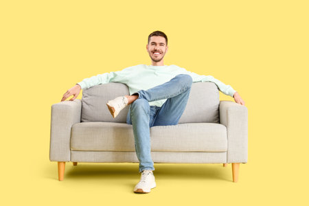 Handsome young happy man resting on sofa against yellow backgroundの写真素材