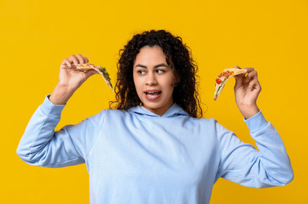 Beautiful young happy African-American woman with slices of delicious pizza on yellow backgroundの写真素材