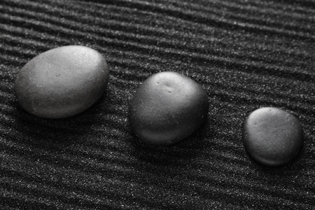 Spa stones on black sand with lines, closeup. Zen concept