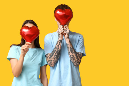 Young couple with heart-shaped air balloons on yellow backgroundの写真素材