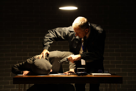 Mature FBI agent threatening suspect with gun in interrogation roomの写真素材