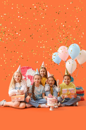 Cute little children in party hats with cake and gifts celebrating Birthday on orange backgroundの写真素材