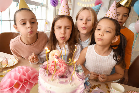 Cute little girls blowing out candles on Birthday cake at party