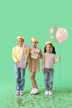 Cute little children in crowns with Birthday gift, cake and balloons on green backgroundの写真素材