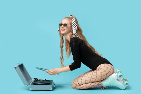 Beautiful young woman in vintage roller skates with record player on blue background