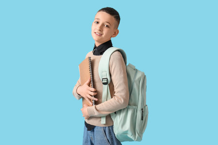 Cute schoolboy with backpack and notebook on blue background