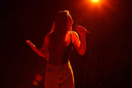 Young woman with modern microphone singing on dark background