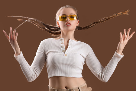 Beautiful young woman with stylish sunglasses posing on brown background