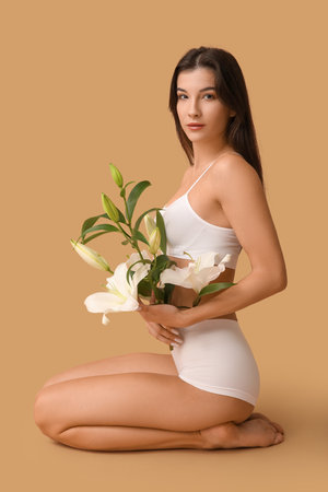 Beautiful young woman with white lily flowers sitting on color backgroundの写真素材
