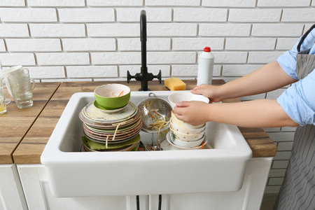 Woman washing dirty dishes in sink near white brick wallの写真素材