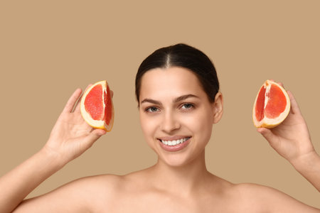 Pretty young woman with fresh grapefruit on beige backgroundの写真素材