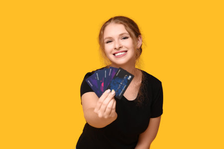 Beautiful young woman with credit cards on yellow backgroundの写真素材