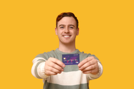 Young man with credit card on yellow backgroundの写真素材