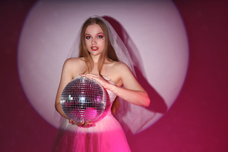 Beautiful young bride with disco ball on color background