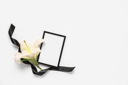Beautiful lily flower with blank frame and black funeral ribbon on white backgroundの写真素材