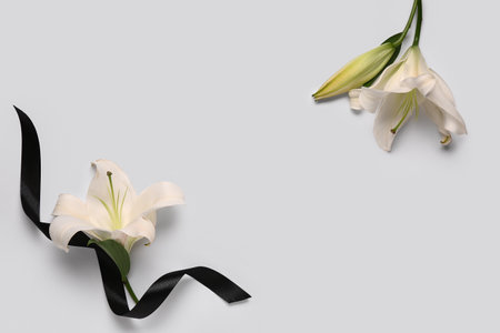 Frame made of beautiful lily flowers with black funeral ribbon on white backgroundの写真素材