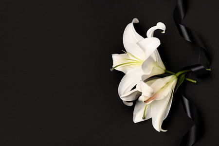 Beautiful lily flowers with black funeral ribbon on dark backgroundの写真素材