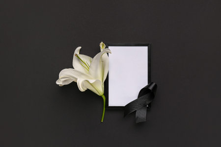 Beautiful lily flower with blank frame and black funeral ribbon on dark backgroundの写真素材