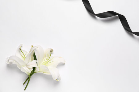 Frame made of beautiful lily flowers with black funeral ribbon on white backgroundの写真素材