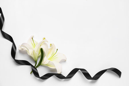 Frame made of beautiful lily flowers with black funeral ribbon on white backgroundの写真素材