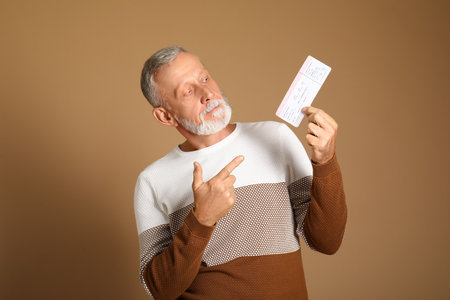 Senior man pointing at ticket on brown backgroundの写真素材