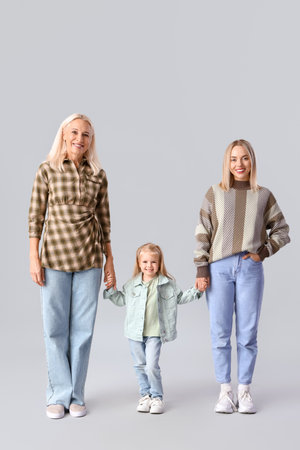 Cute little girl with her mother and granny holding hands on light backgroundの写真素材