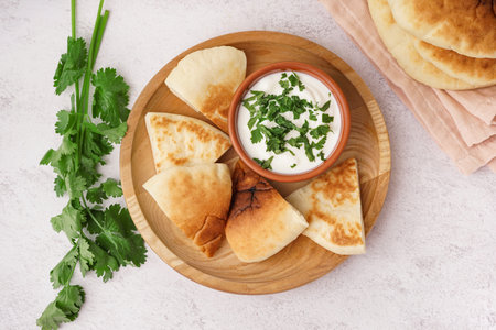 Plate with pieces of tasty pita bread and sauce on white background