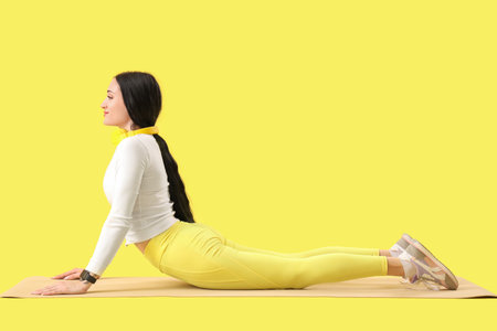Portrait of sporty young woman practicing pilates on yoga mat against yellow background