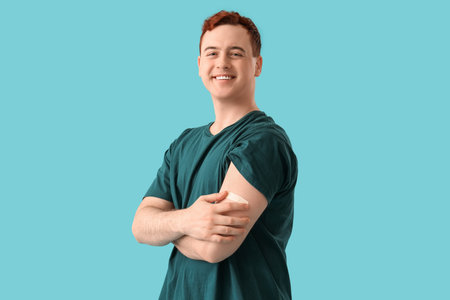 Happy young man with applied medical patch on blue background. Vaccination conceptの写真素材