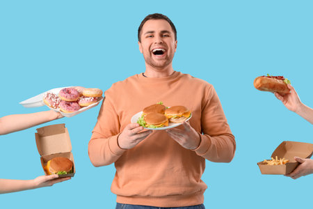 Young man and hands with unhealthy food on blue background. Overeating conceptの写真素材