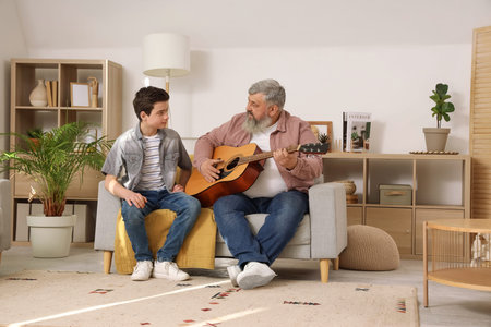 Happy grandfather with his cute grandson playing guitar at home