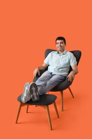 Young man sitting in armchair with footrest on red backgroundの写真素材