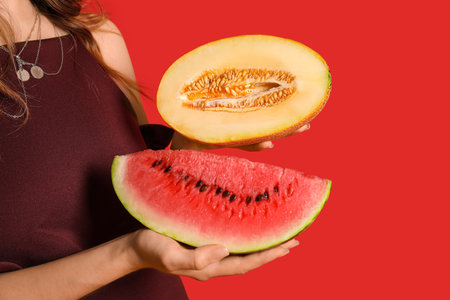 Beautiful young woman with fresh watermelon and melon on red background, closeupの写真素材